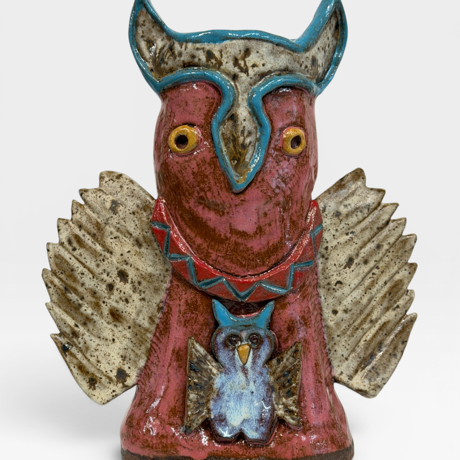 A rustic ceramic owl figurine with a reddish-brown body, textured speckled wings in beige and brown, and turquoise blue accents on the head, collar, and smaller owl detail on the front, set against a plain light gray background.