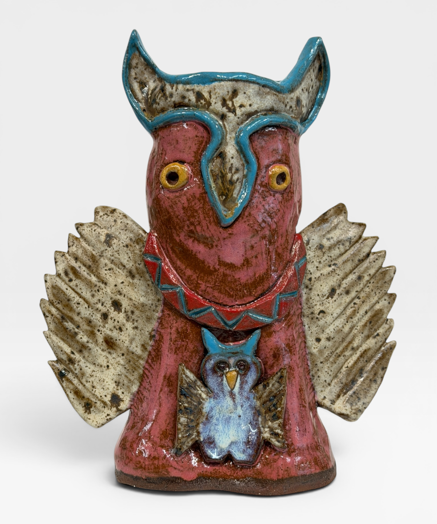A rustic ceramic owl figurine with a reddish-brown body, textured speckled wings in beige and brown, and turquoise blue accents on the head, collar, and smaller owl detail on the front, set against a plain light gray background.