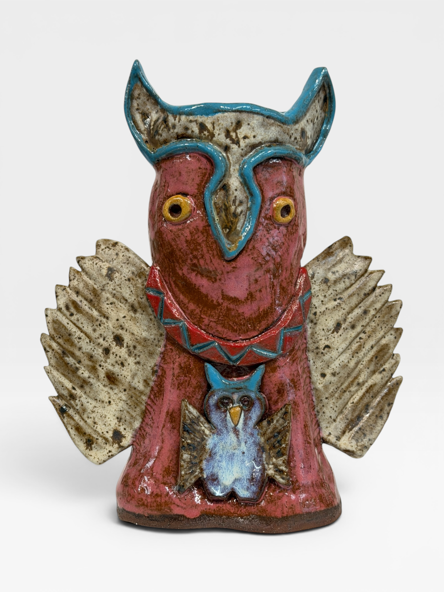 A rustic ceramic owl figurine with a reddish-brown body, textured speckled wings in beige and brown, and turquoise blue accents on the head, collar, and smaller owl detail on the front, set against a plain light gray background.